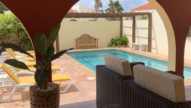 Un espacio al aire libre techado con piscina, sillas de descanso y un sofá de mimbre.