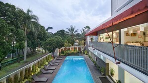 A swimming pool with sun loungers, surrounded by greenery and a building with a red awning. - Grand Cakra Hotel (Malang)
