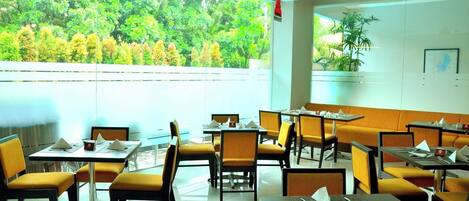 A restaurant with outdoor seating, tables, chairs, and a view of greenery.