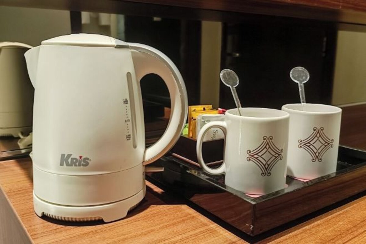 Uma cafeteira Krism branca, duas chávenas brancas com desenhos decorativos e uma colher sobre um alçapão.