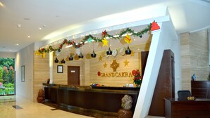 A reception area with a wooden reception desk, a large sign reading "Grand Cakra", and a decorative garland above the desk. - Grand Cakra Hotel (Malang)
