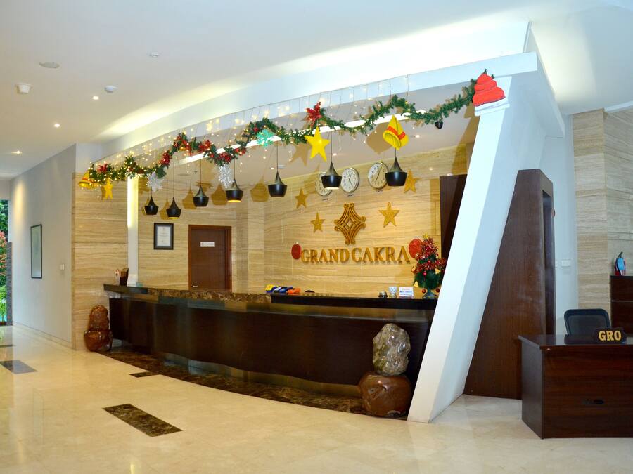 A reception area with a wooden reception desk, a large sign reading "Grand Cakra", and a decorative garland above the desk.