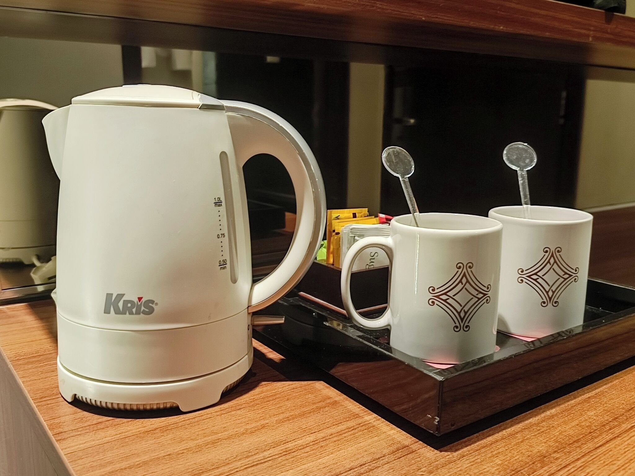 A white Krups coffee maker on a wooden tray with two white mugs with decorative patterns.