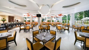 A spacious restaurant with a modern design, featuring a central seating area with tables and chairs, a buffet counter on the left, and large windows providing views of the outdoors. - Grand Cakra Hotel (Malang)