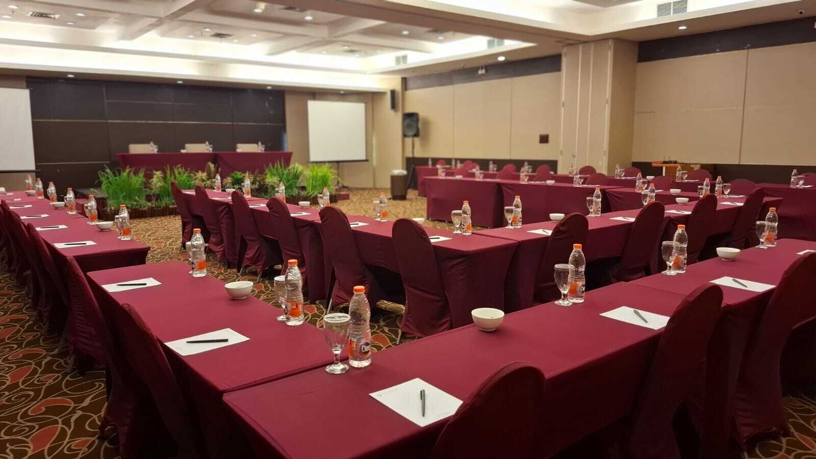 A conference room with long tables, chairs, water bottles, and a projector screen.