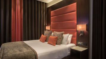 Een moderne hotelkamer met een groot bed, een houten hoofdbord, twee bedlampjes en een nachtkastje met bedieningspaneel.