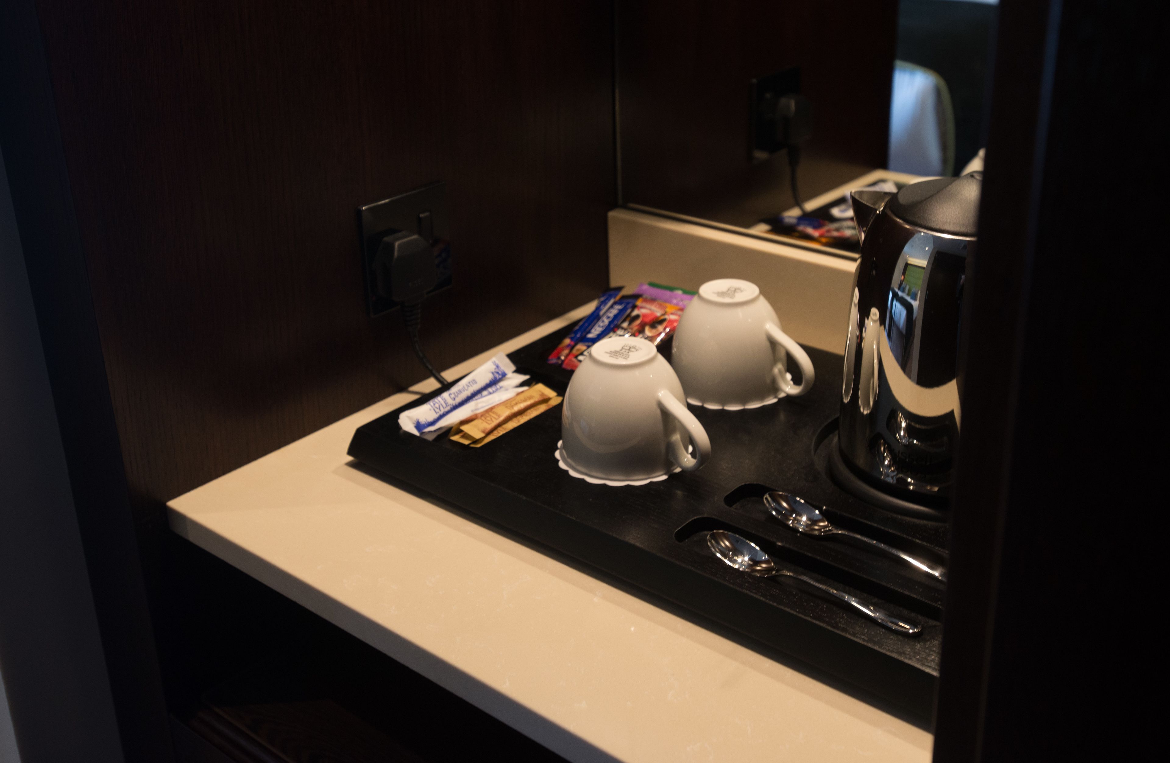 Ein Frühstücksbereich in einem Hotelzimmer mit einer Kaffeemaschine, zwei weißen Tassen und einzelnen Speisen auf einem Tablett.