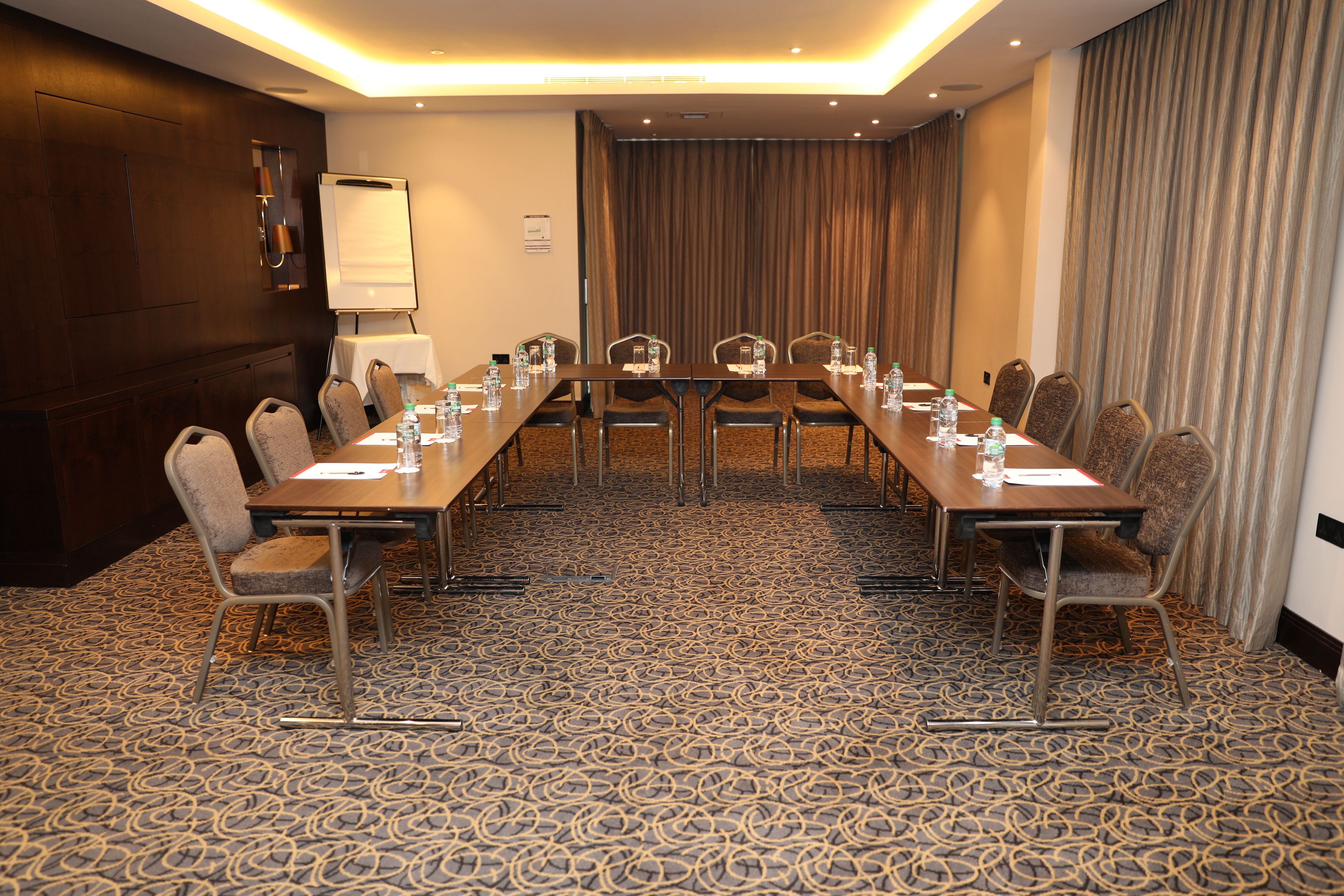 A conference room with a long table, chairs, a whiteboard, and a projector screen.