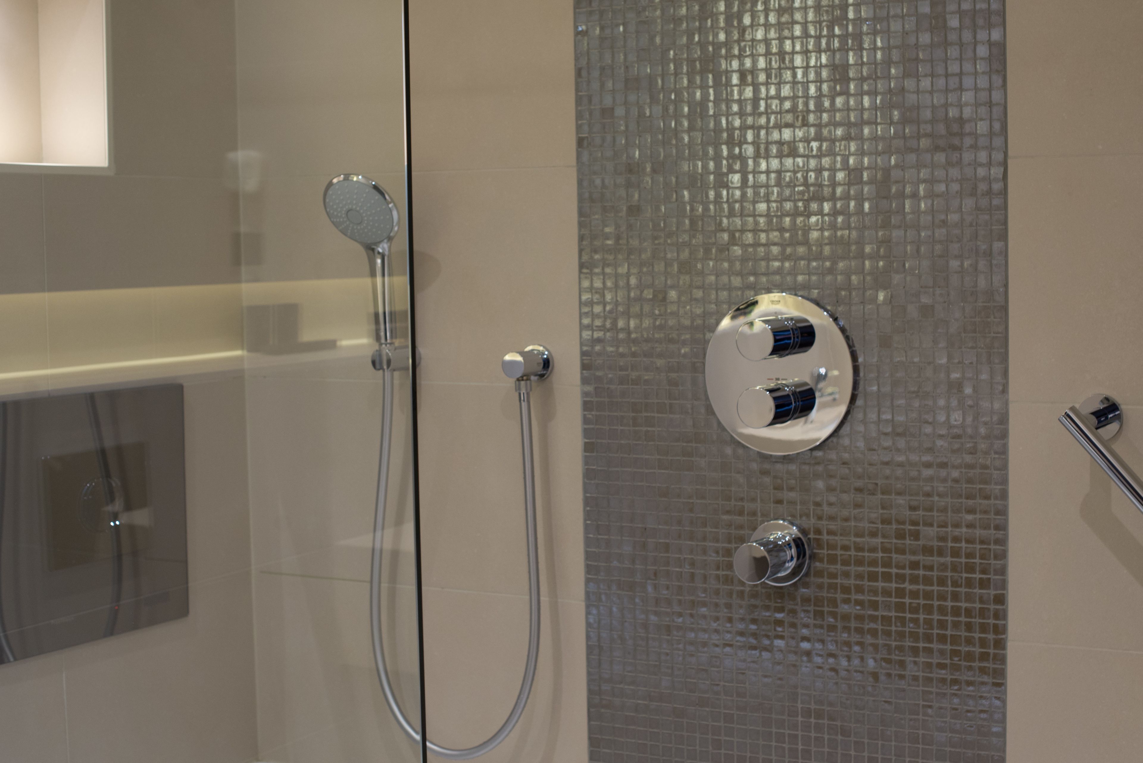 A modern bathroom with a glass shower enclosure, a handheld showerhead, and a wall-mounted control panel.