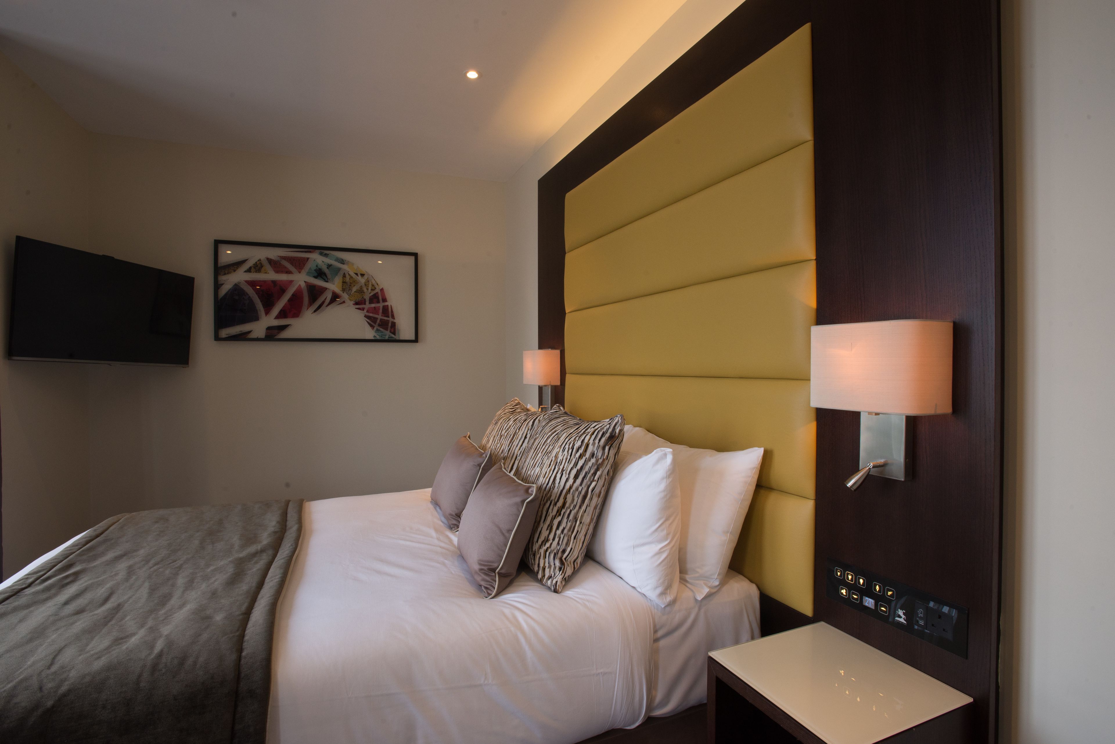 Hotelkamer met een bed, twee bedlampen, een flatscreen televisie en een bedieningspaneel aan de muur.
