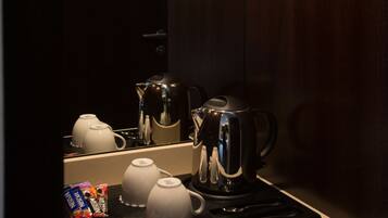 A compact kitchen with a coffee maker, teapots, and a glass shelf holding wine glasses.