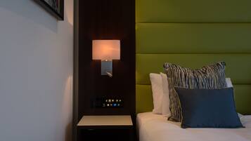 A hotel room with a bed, a nightstand, a wall-mounted lamp, and a green headboard.