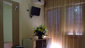 A hotel room with a bed, a desk with a chair, a TV, and a window with curtains.
