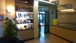 A reception area with a reception desk, a plant, and a display of various items on shelves.