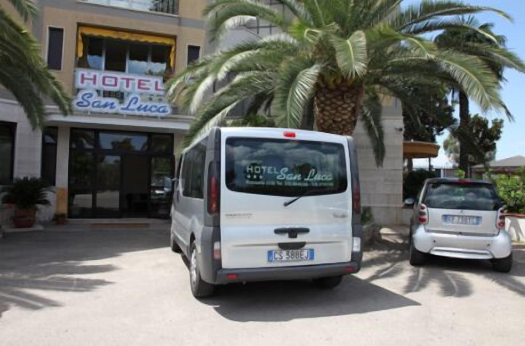 Una furgoneta blanca aparcada davant d'un hotel anomenat "HOTEL San Luca", amb matrícula visible.