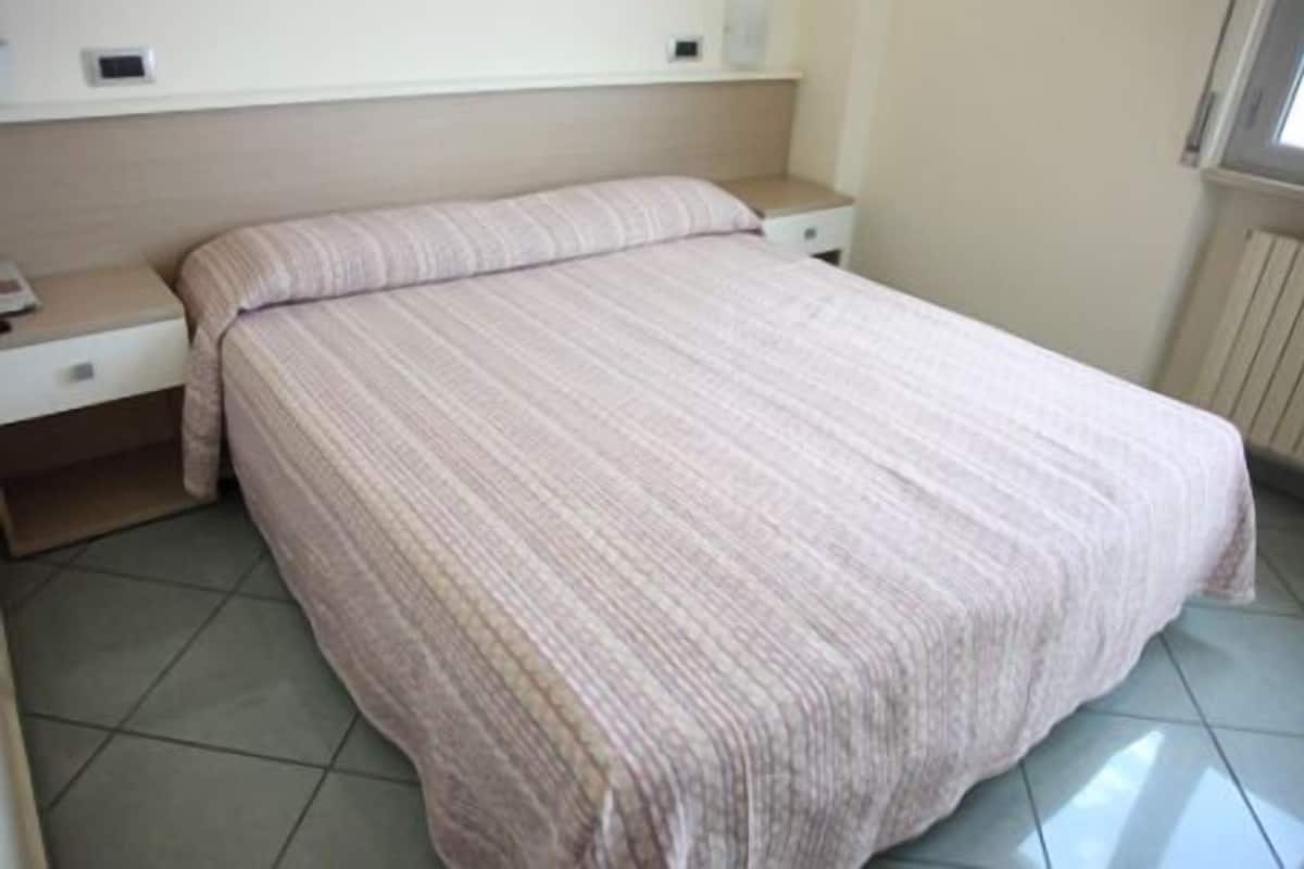 A bedroom with a bed, a nightstand, a drawer, and a window.
