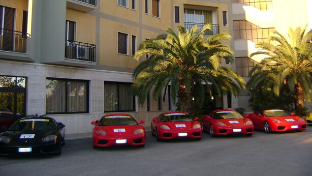 A multi-story hotel with balconies, parked sports cars, and palm trees.