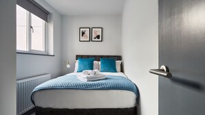 Un letto rifatto con una coperta blu, due cuscini e un asciugamano piegato. Sopra il letto, sulla parete, due quadri.
