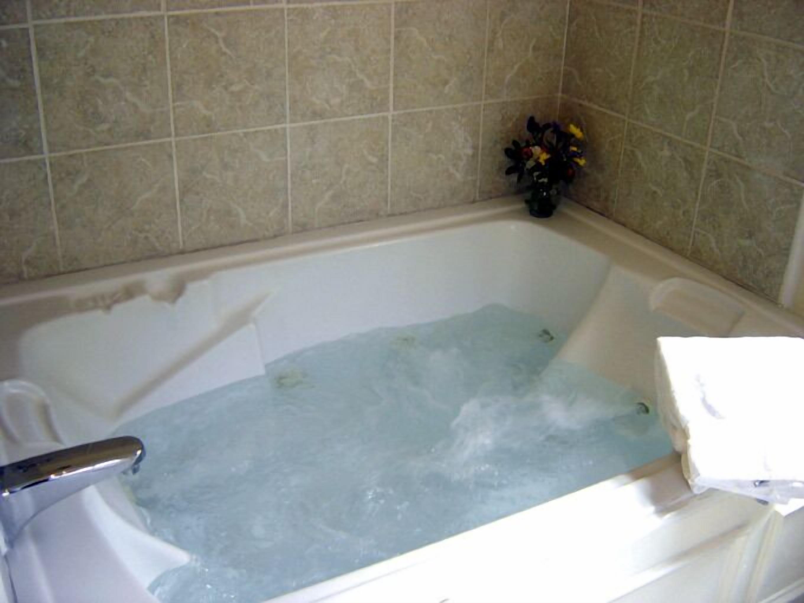 Una bañera con agua, un florero y una toalla sobre una superficie blanca.