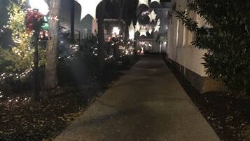 Un camino bordeado de árboles y decoraciones con forma de estrella, que conduce a un edificio de fachada de ladrillo.