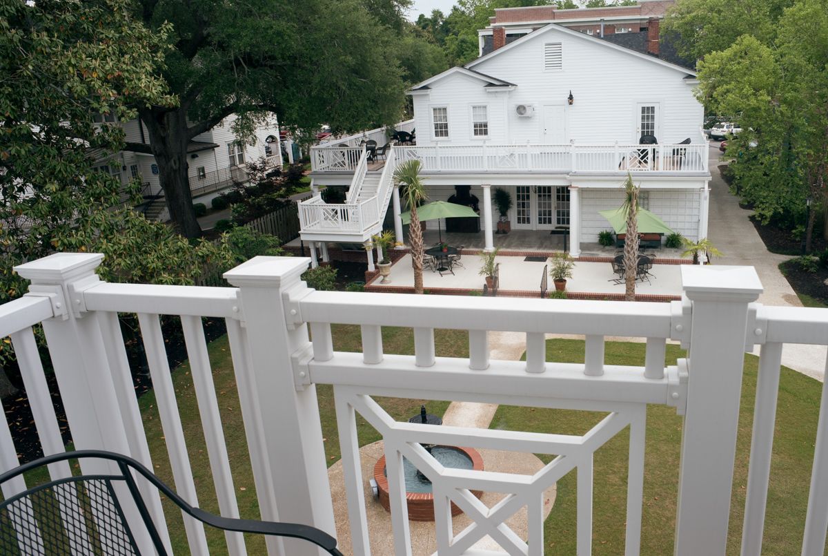A white two-story house with a balcony, a small fountain, and a covered patio area.