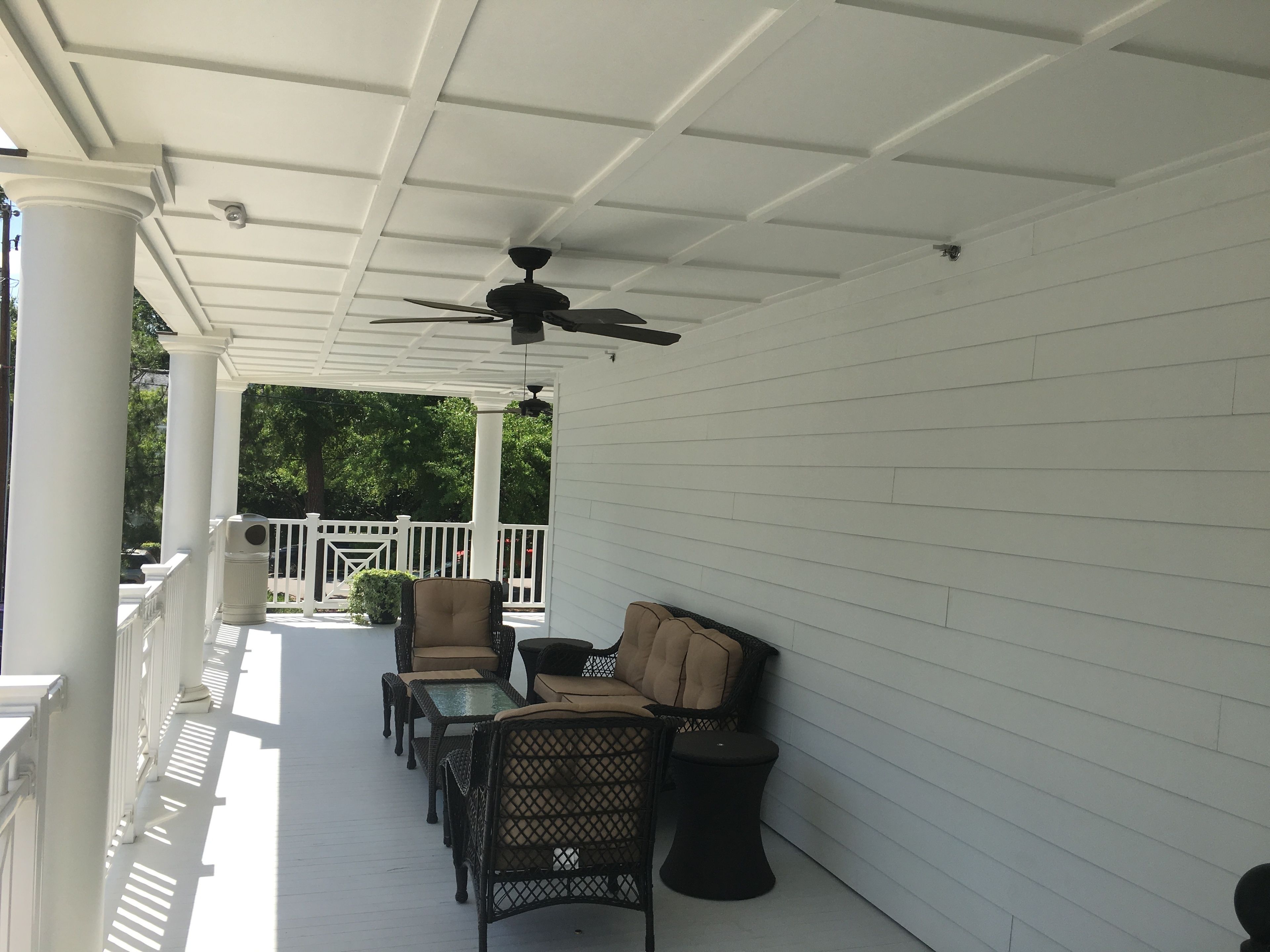 A covered porch with white columns, a ceiling fan, and outdoor furniture including chairs and a table.