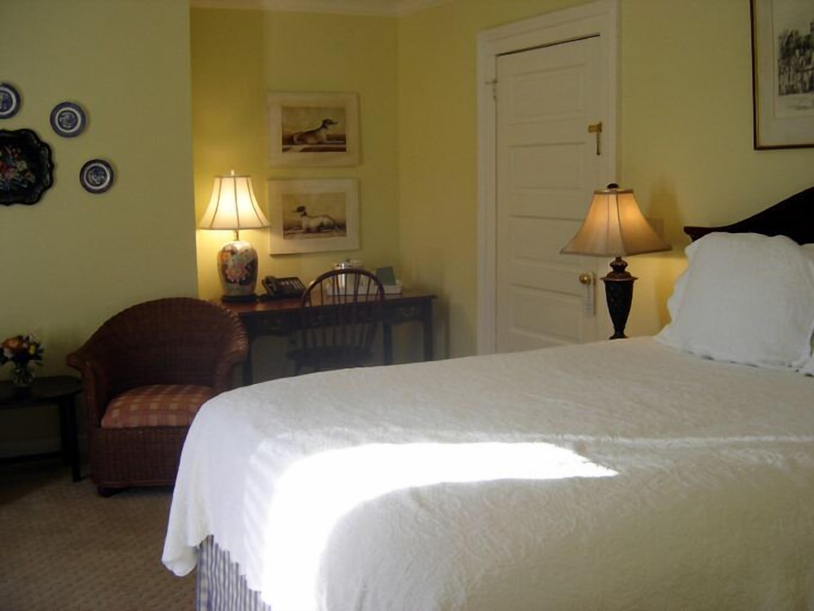 Une chambre à coucher avec un lit, deux lampes, une chaise, un bureau et une porte.