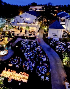 An outdoor dining area with multiple tables and chairs, surrounded by buildings and a pool.