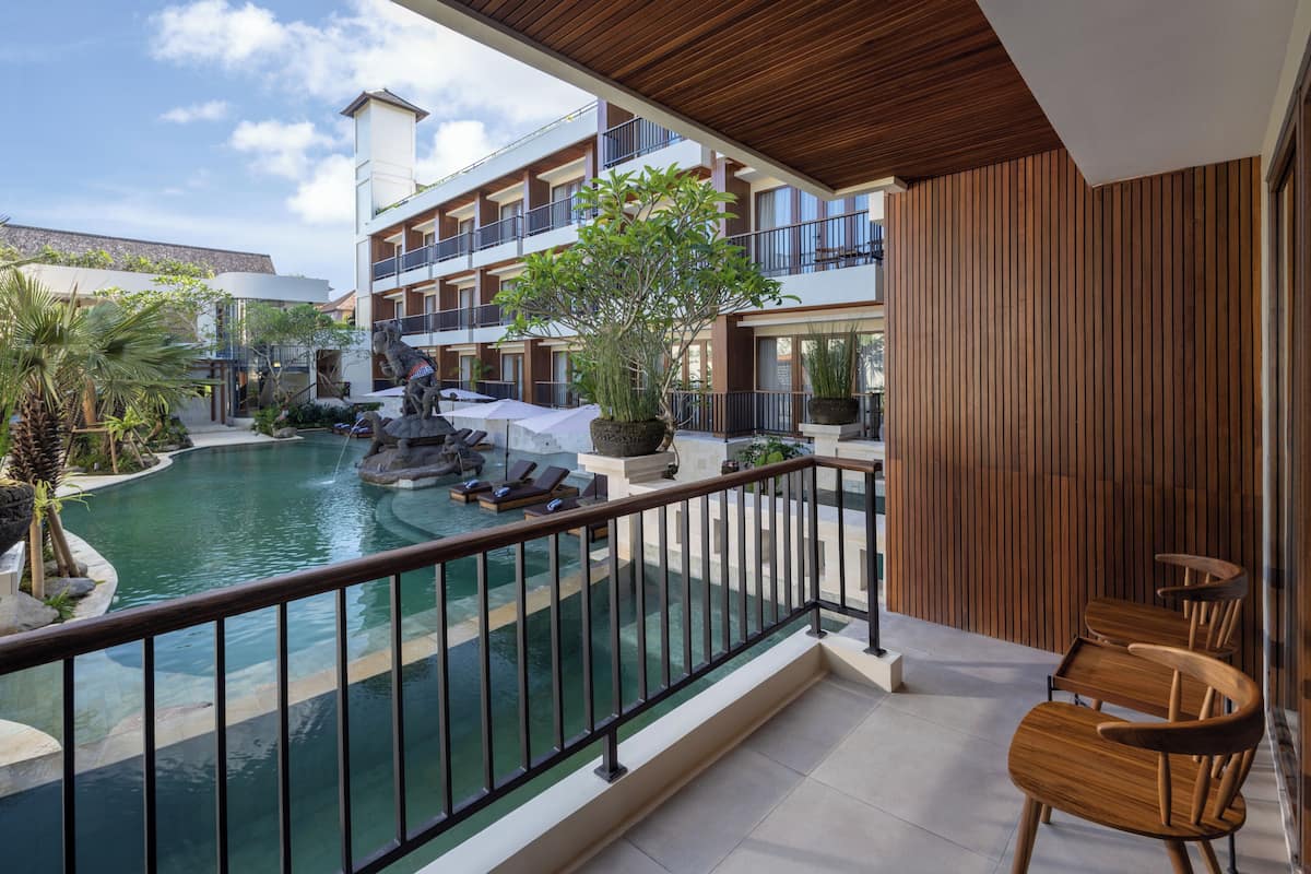 A pool area with lounge chairs, a wooden deck, and a view of a multi-story building.