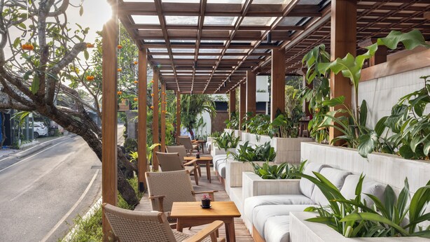 A covered outdoor seating area with wooden furniture, potted plants, and a view of a road. - Anumana Ubud Bali (Ubud)