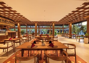 A restaurant with wooden tables and chairs, a bar area, and large windows with a view of greenery.