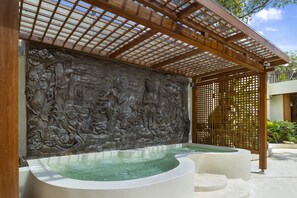 A spa area with a stone wall relief, a wooden pergola, and a pool.