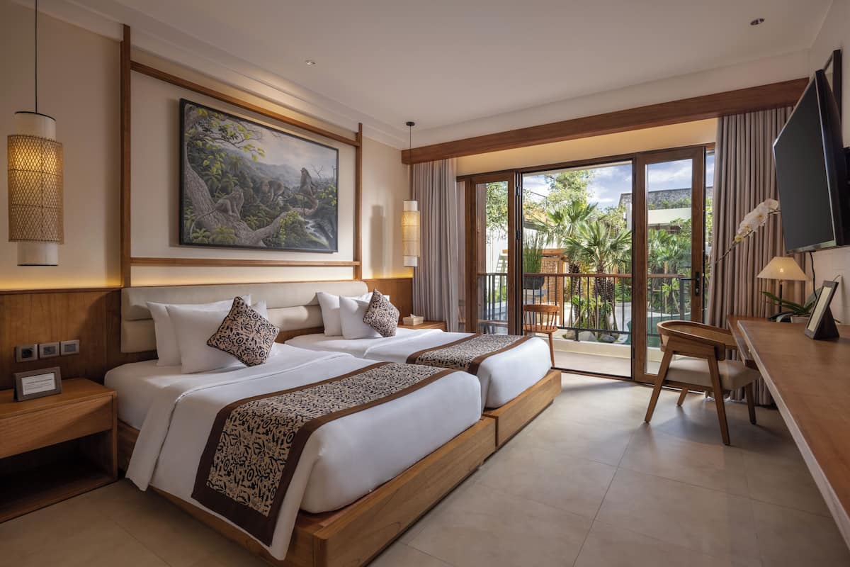 A hotel room with two beds, a desk, a TV, a painting, and a balcony with a view.