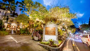 A well-lit street with a sign reading "ANUMANA" and a stone monument surrounded by greenery. - Anumana Ubud Bali (Ubud)