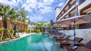 A swimming pool with lounge chairs and umbrellas, surrounded by greenery and a building with balconies. - Anumana Ubud Bali (Ubud)