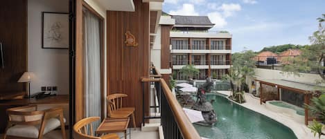 Un balcón con muebles de madera, una piscina y vistas a un edificio con varios balcones.