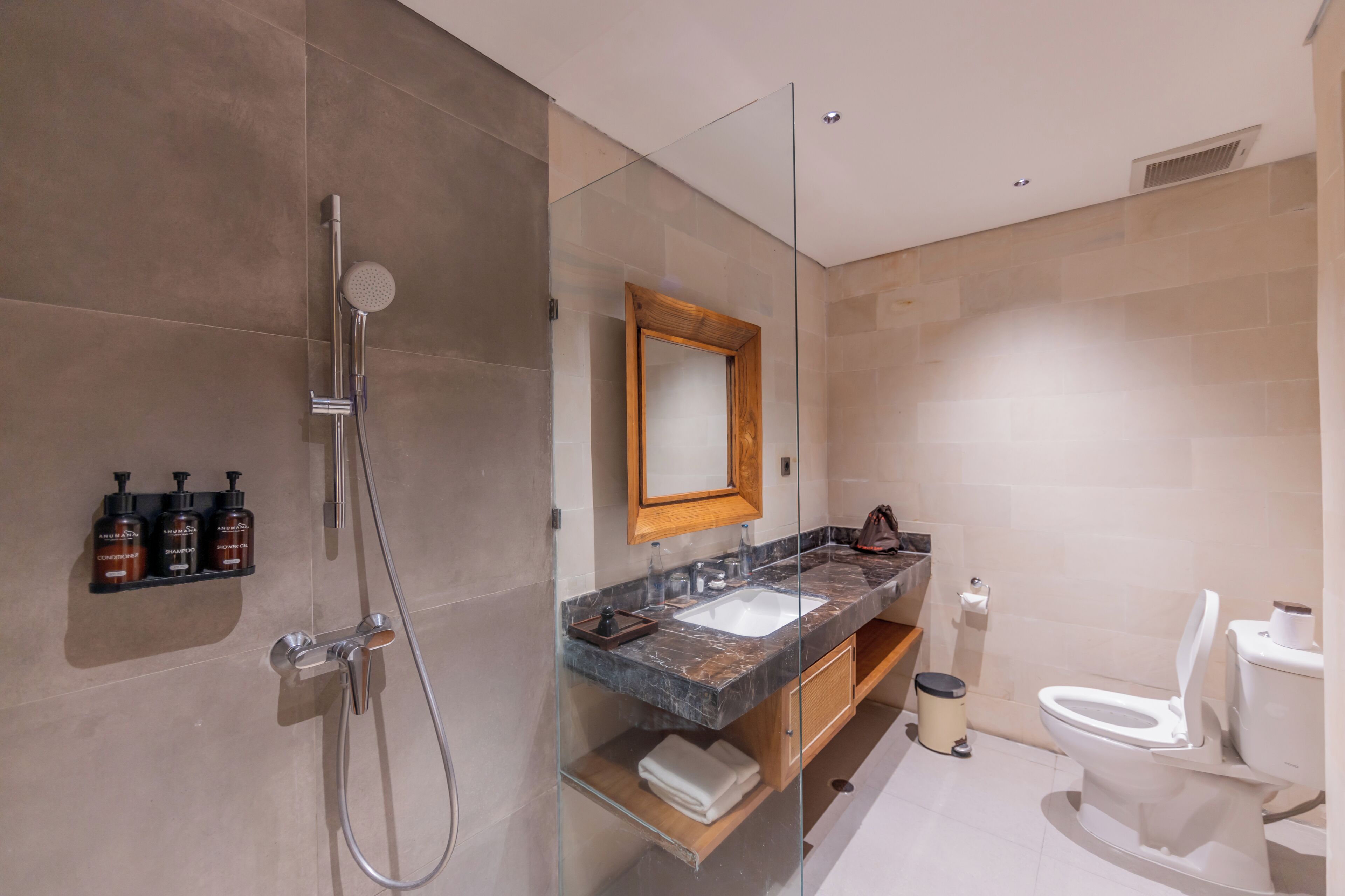 A modern bathroom with a glass shower enclosure, a wooden-framed mirror, a marble sink, and a toilet.
