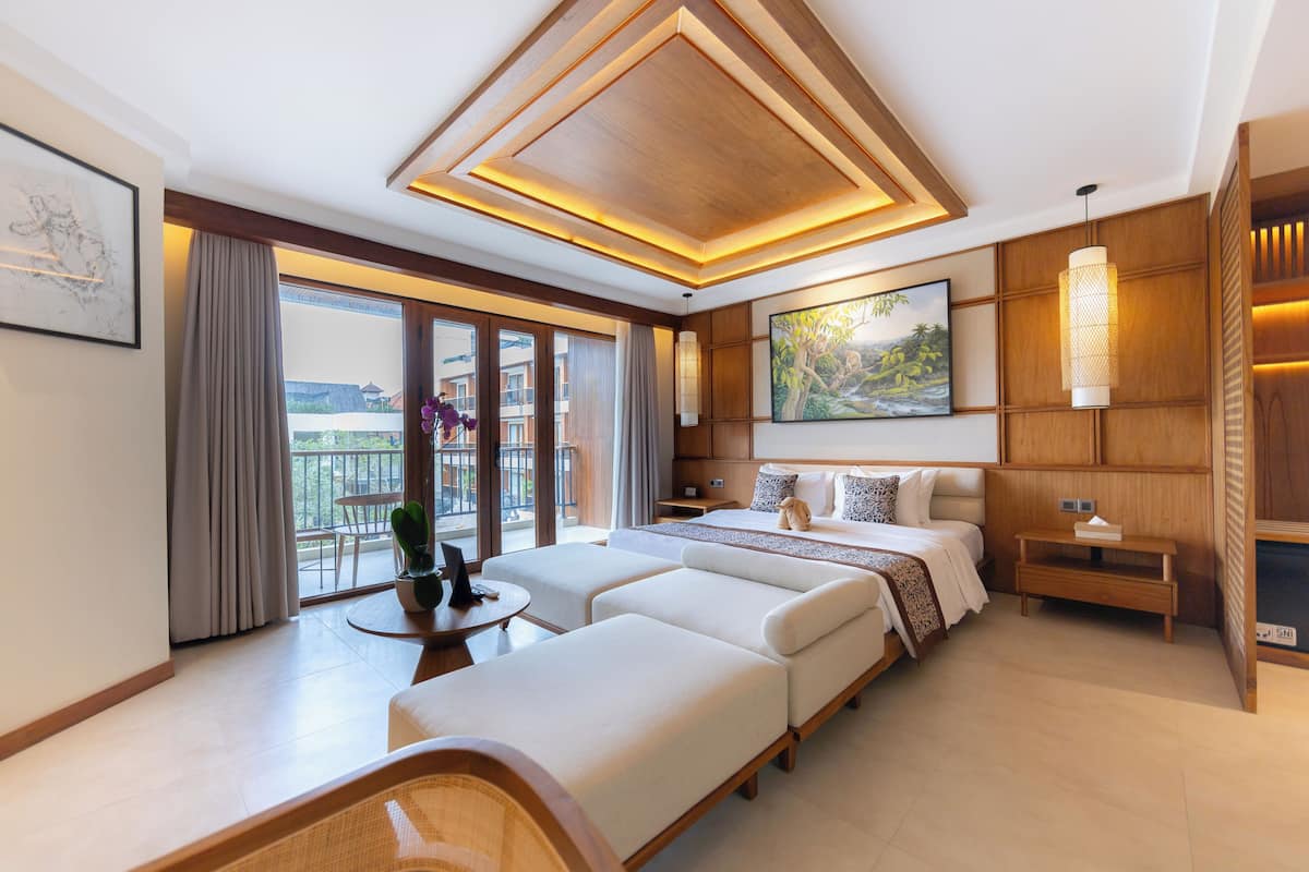 A modern hotel room with a large bed, two sofas, a small table, and a balcony with curtains.
