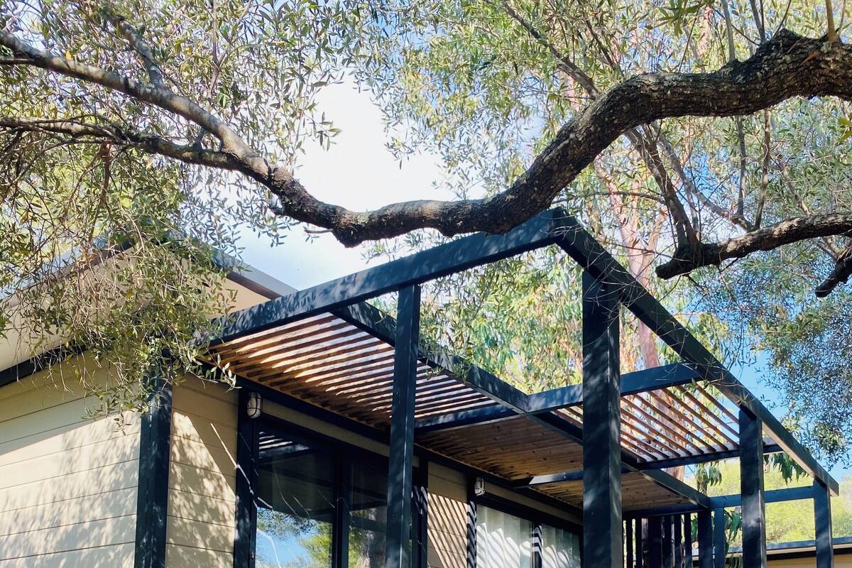 Un espace extérieur abrité, aménagé avec des sièges, et un escalier en bois menant à un bâtiment portant l’inscription « Gitotel ».