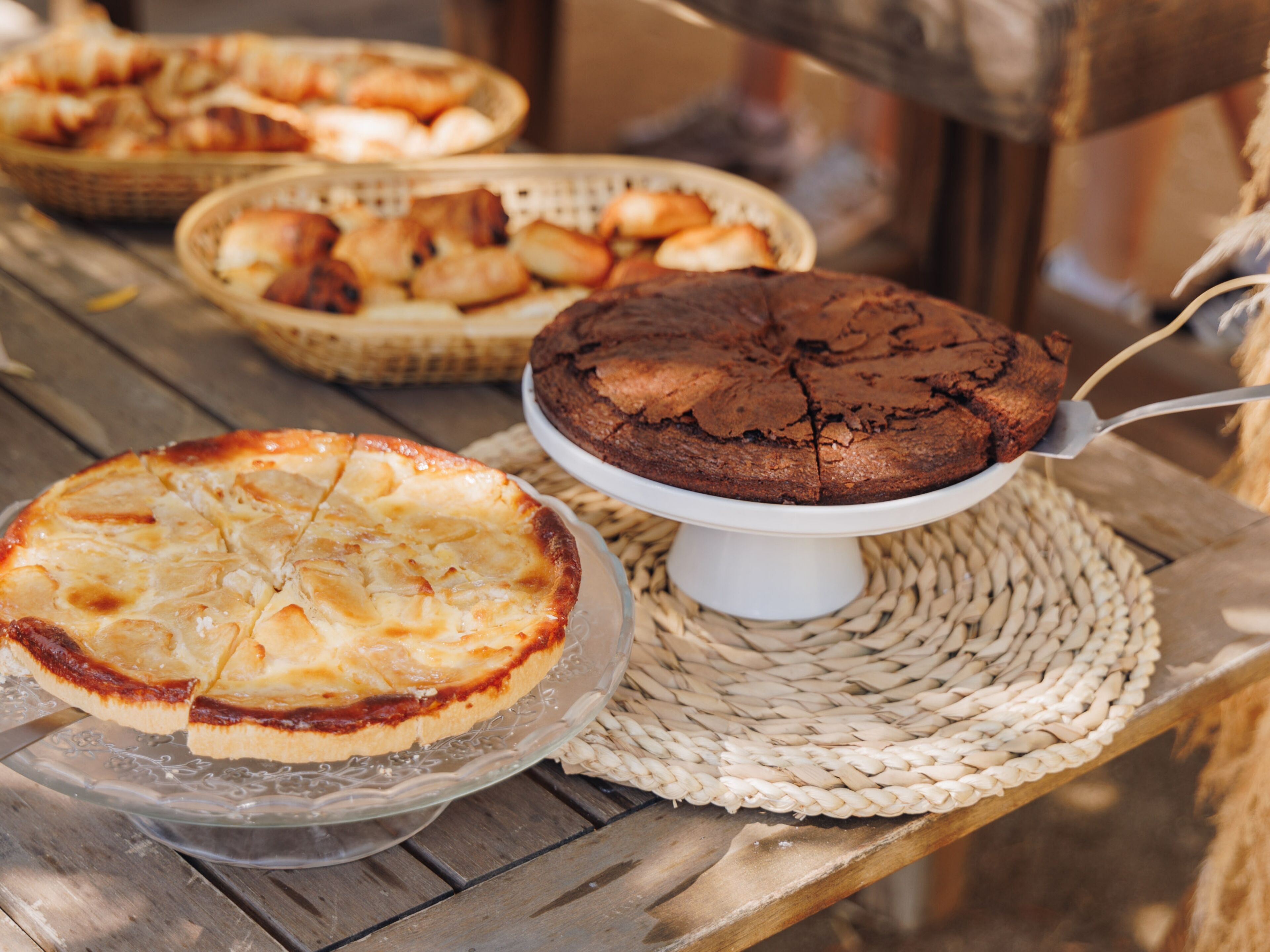 A wooden table with three different types of baked goods: a pie, a cake, and a loaf of bread.