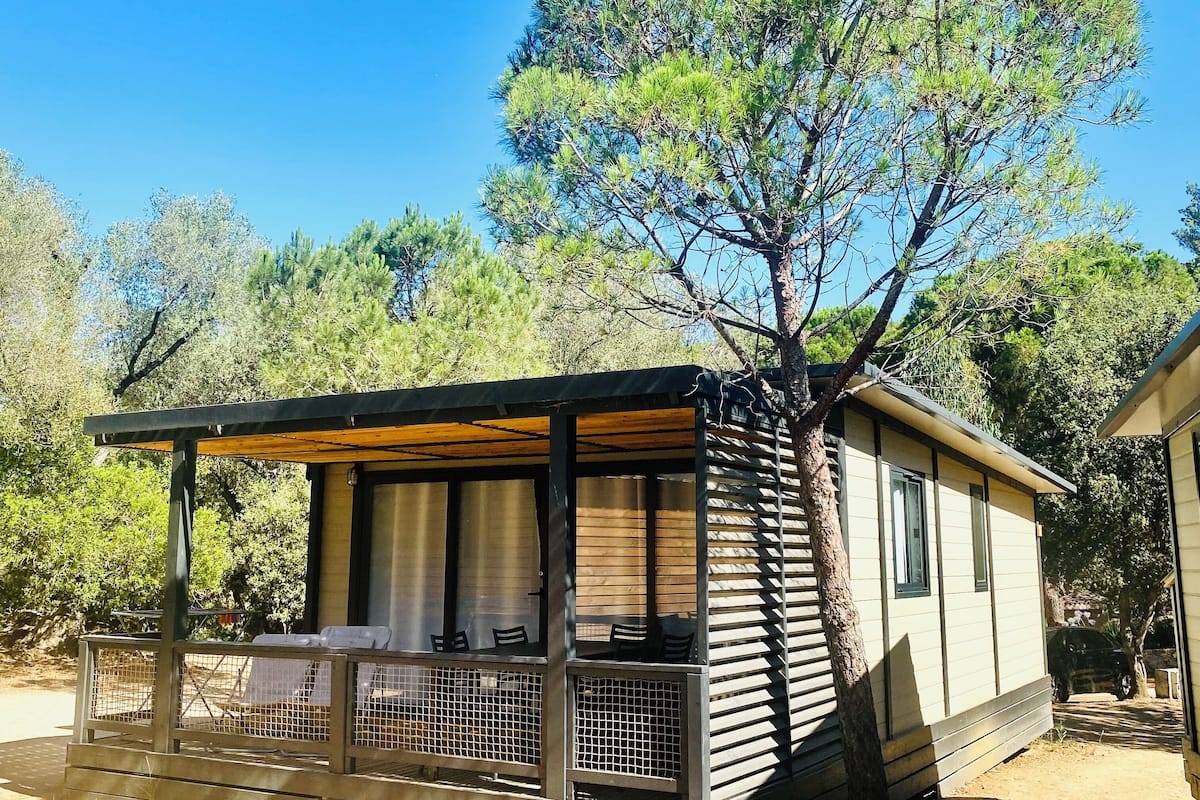 Une petite cabane dotée d’un porche abrité, d’un coin repas et d’un grand arbre à l’avant.
