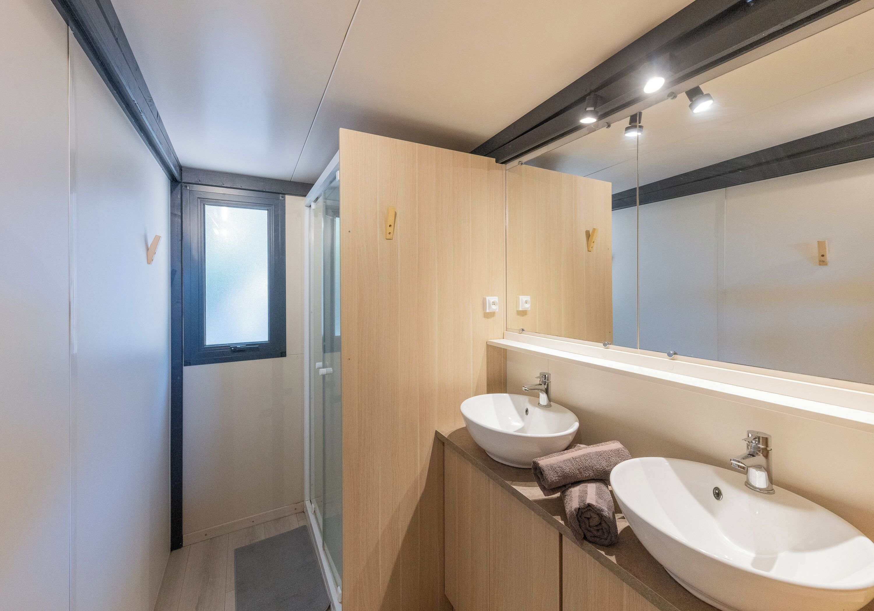 Un baño moderno con cabina de ducha de vidrio, dos lavamanos y un espejo grande.