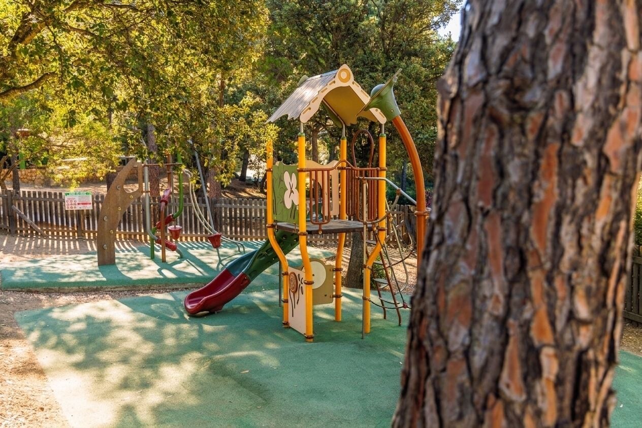Un parque infantil con tobogán, estructuras para escalar y un árbol en primer plano.