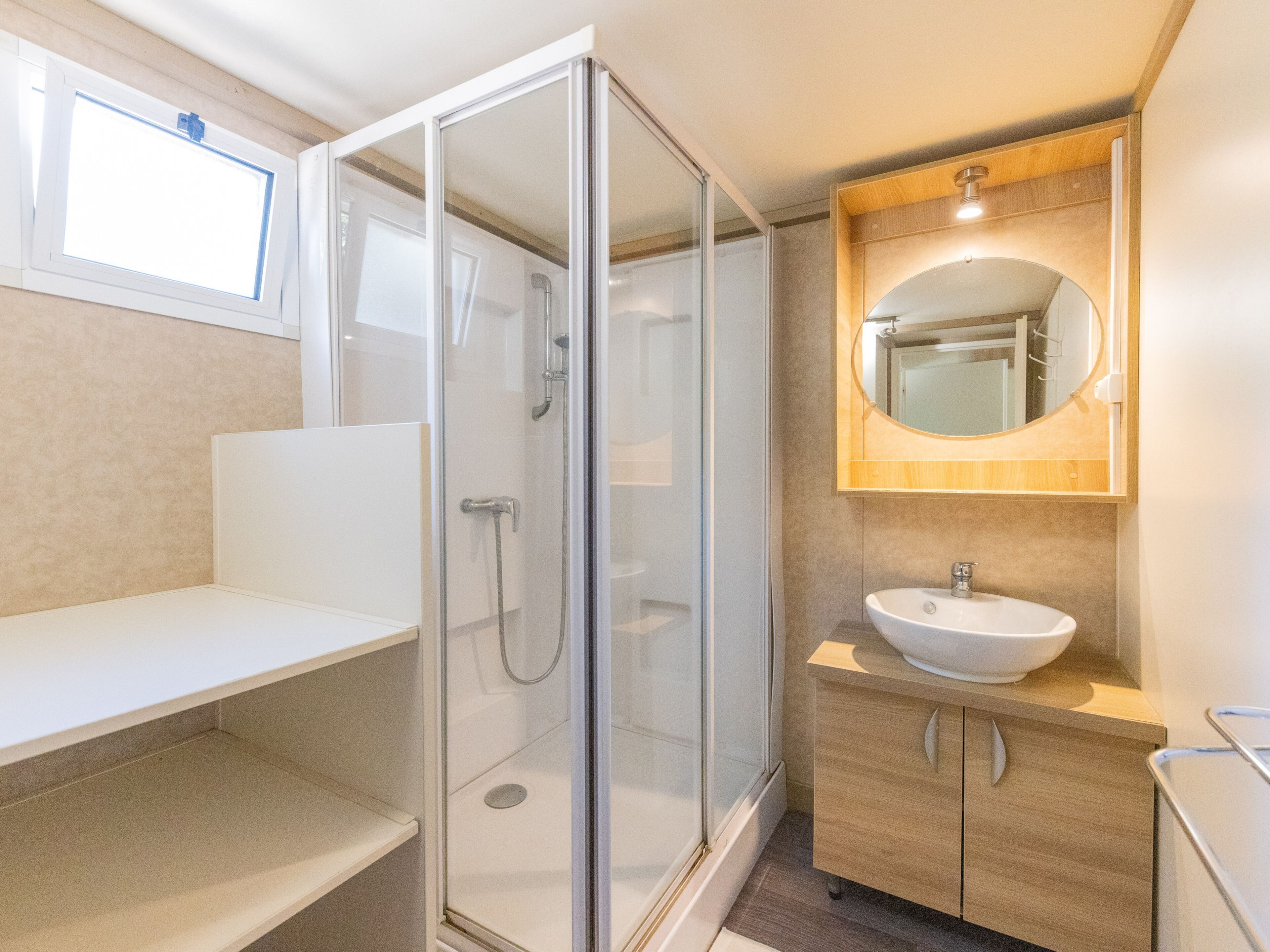 A modern bathroom with a glass shower enclosure, a wooden vanity with a sink, and a mirror.