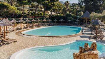 Una piscina con sillas de descanso y sombrillas, rodeada de árboles y un sendero de piedra.