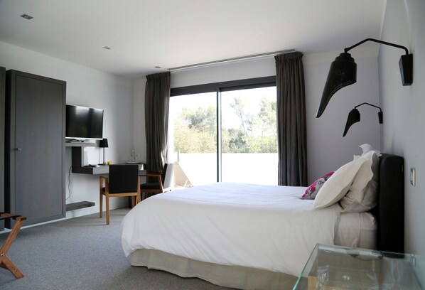 A modern hotel room with a large bed, a desk with a chair, a television, and a large window with curtains.