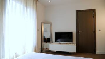 A hotel room with a bed, a TV on a white dresser, a door, and a window with curtains.