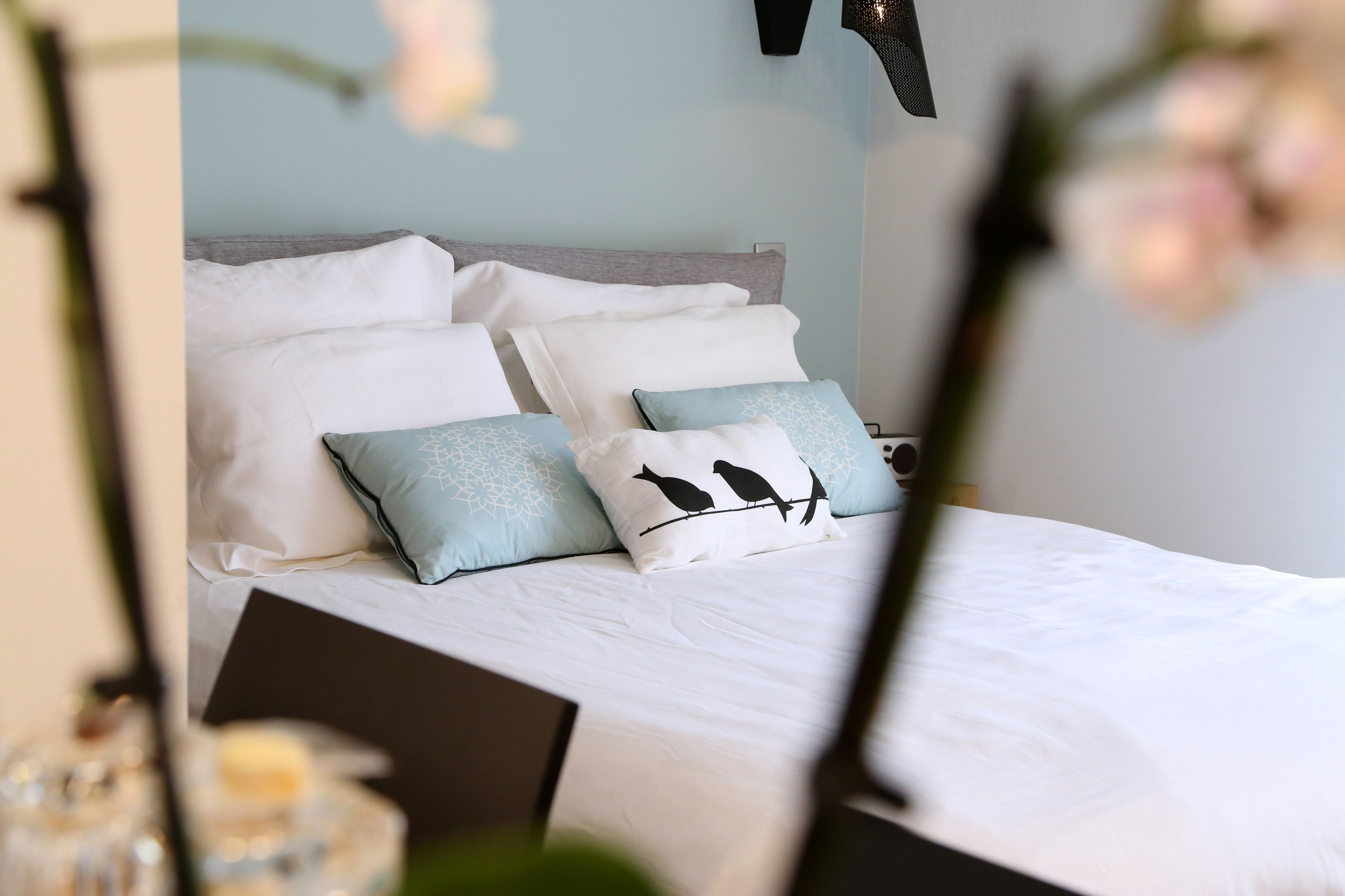 A neatly made bed with white bedding and decorative pillows, including one with a bird design.