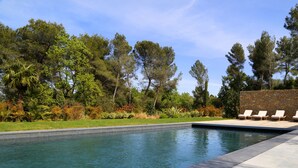 A swimming pool with a stone wall and lounge chairs. - Domaine Rampale (Fuveau)