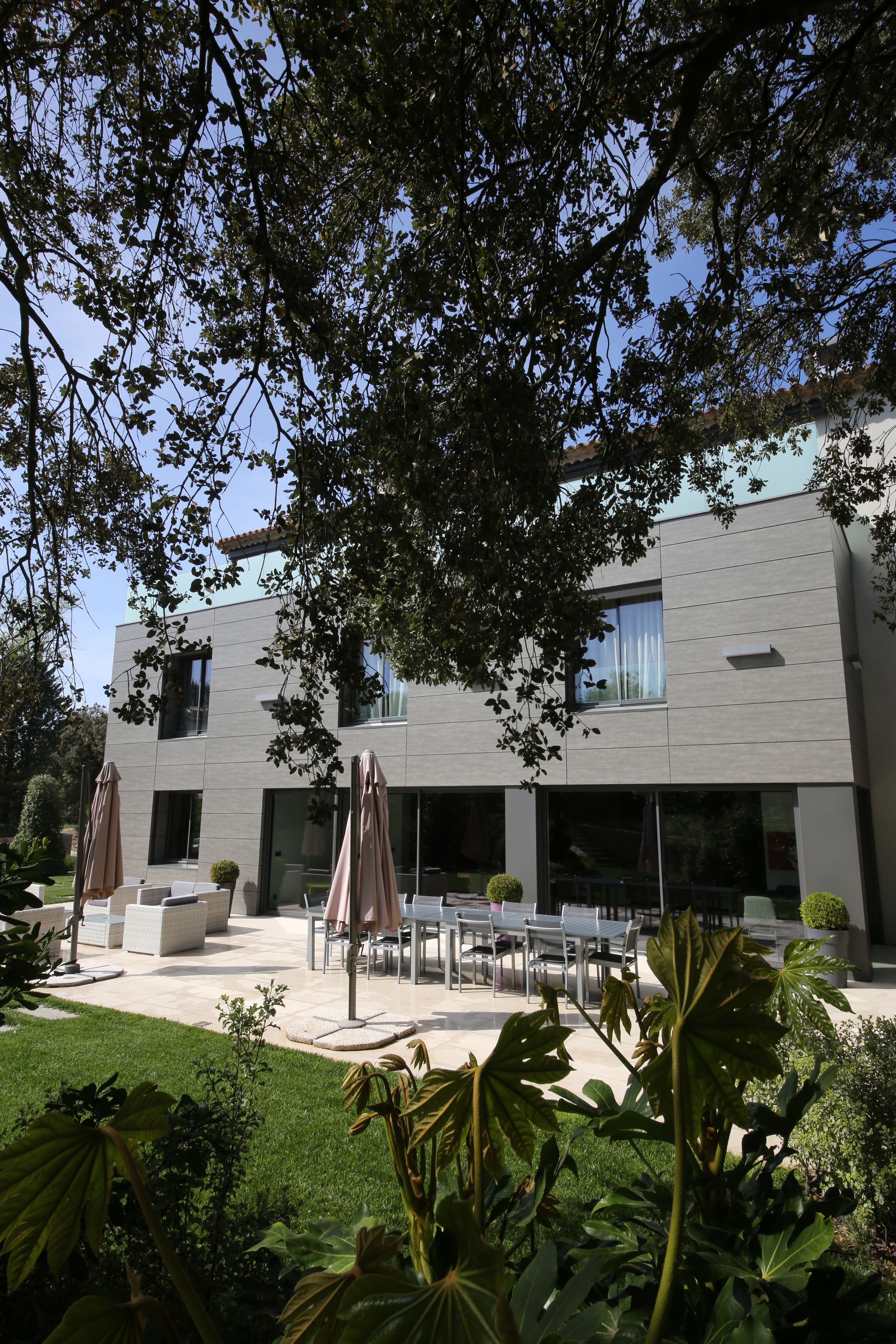 A modern building with a patio area featuring outdoor furniture and umbrellas.